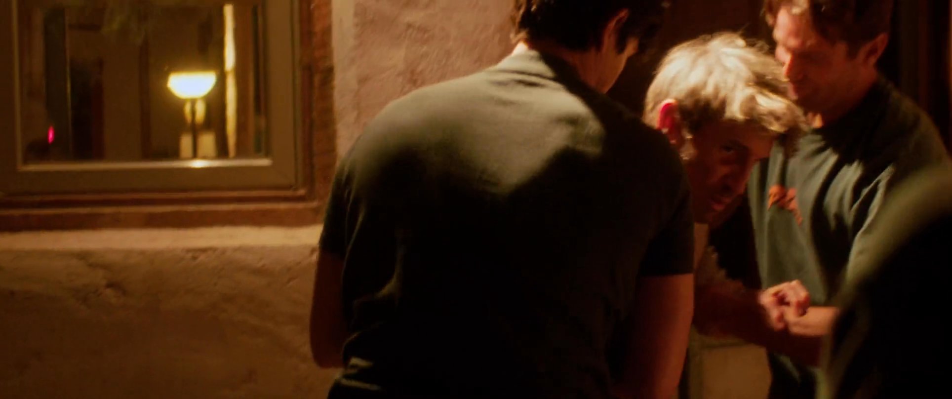 Two men physically restrain a third individual during a heated domestic altercation, while a woman observes the tense scene with a serious expression.