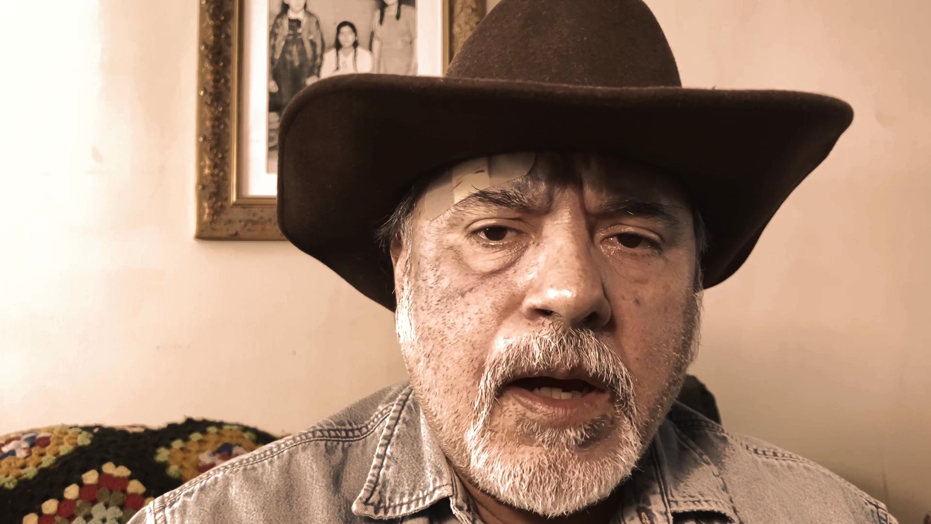 A man wearing a cowboy hat delivers a focused monologue while facing the camera. He maintains a serious expression in an indoor setting.