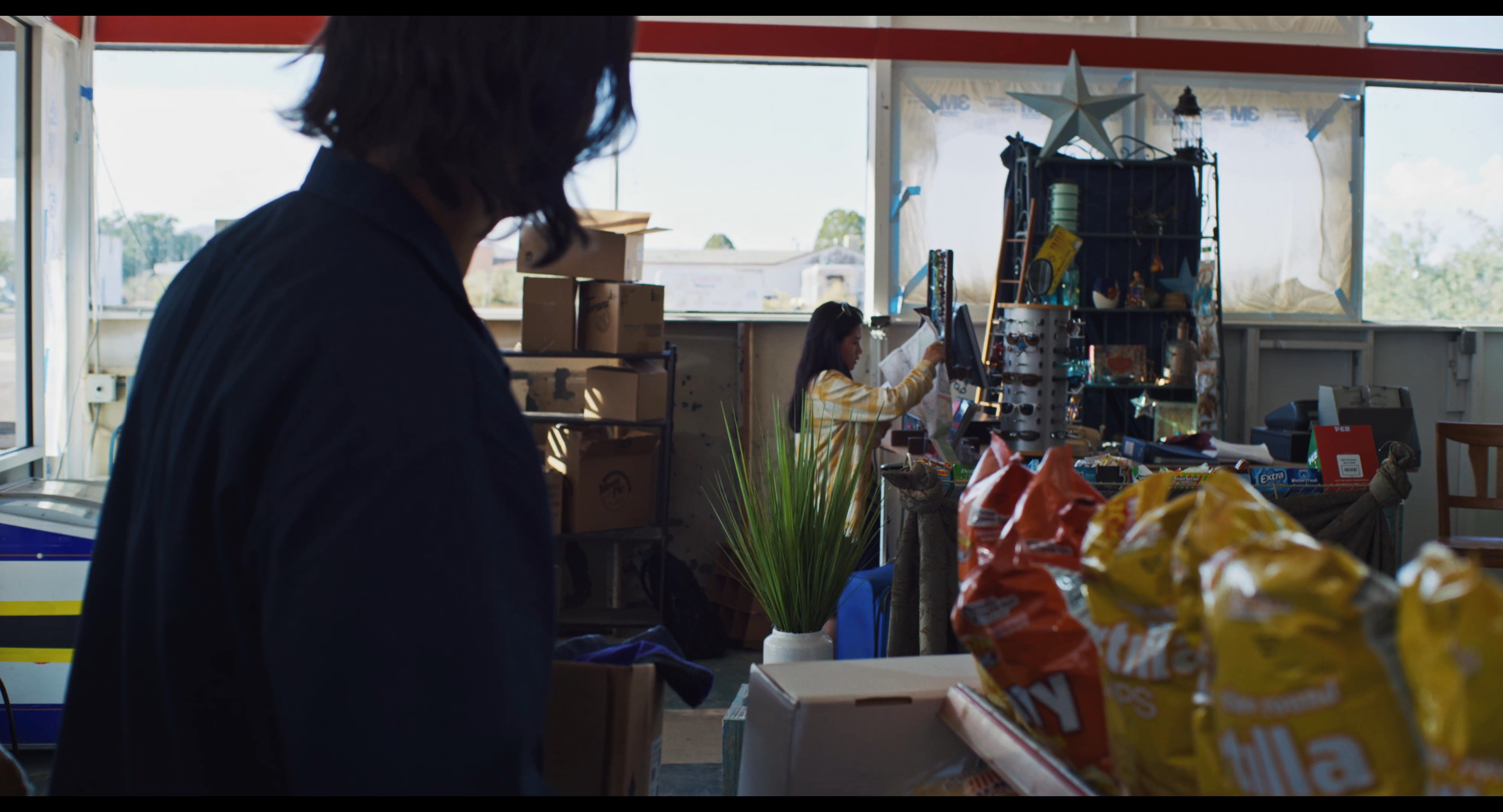 An employee systematically replenishes snack inventory on store shelves while a customer reviews merchandise nearby. This activity highlights routine operational tasks within a commercial retail environment.