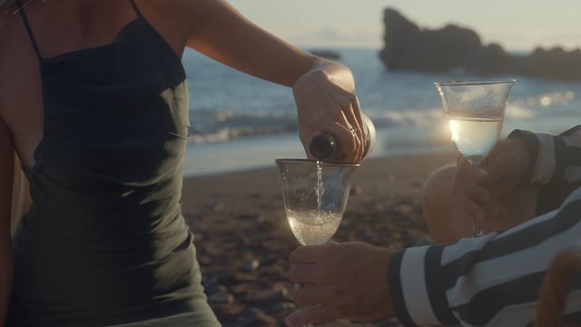 A woman pouring champagne into glasses at sunset on the beach