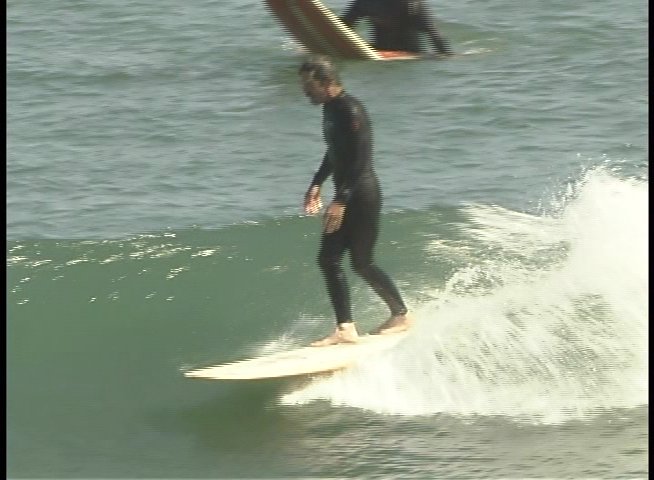 A surfer wearing a wetsuit maintains balance while carving and riding a rolling ocean wave on a longboard.
