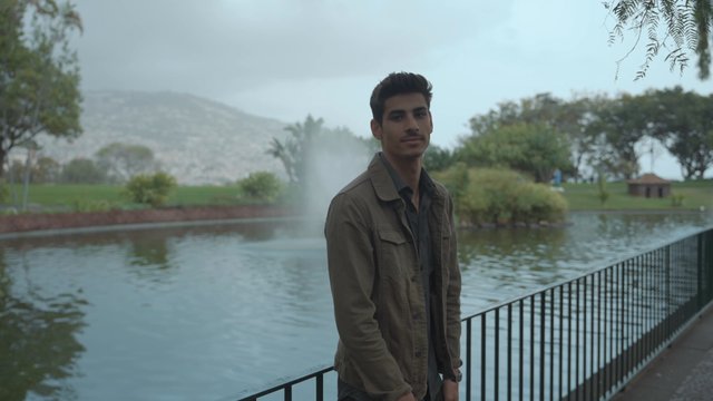 A guy standing near a pond in a park