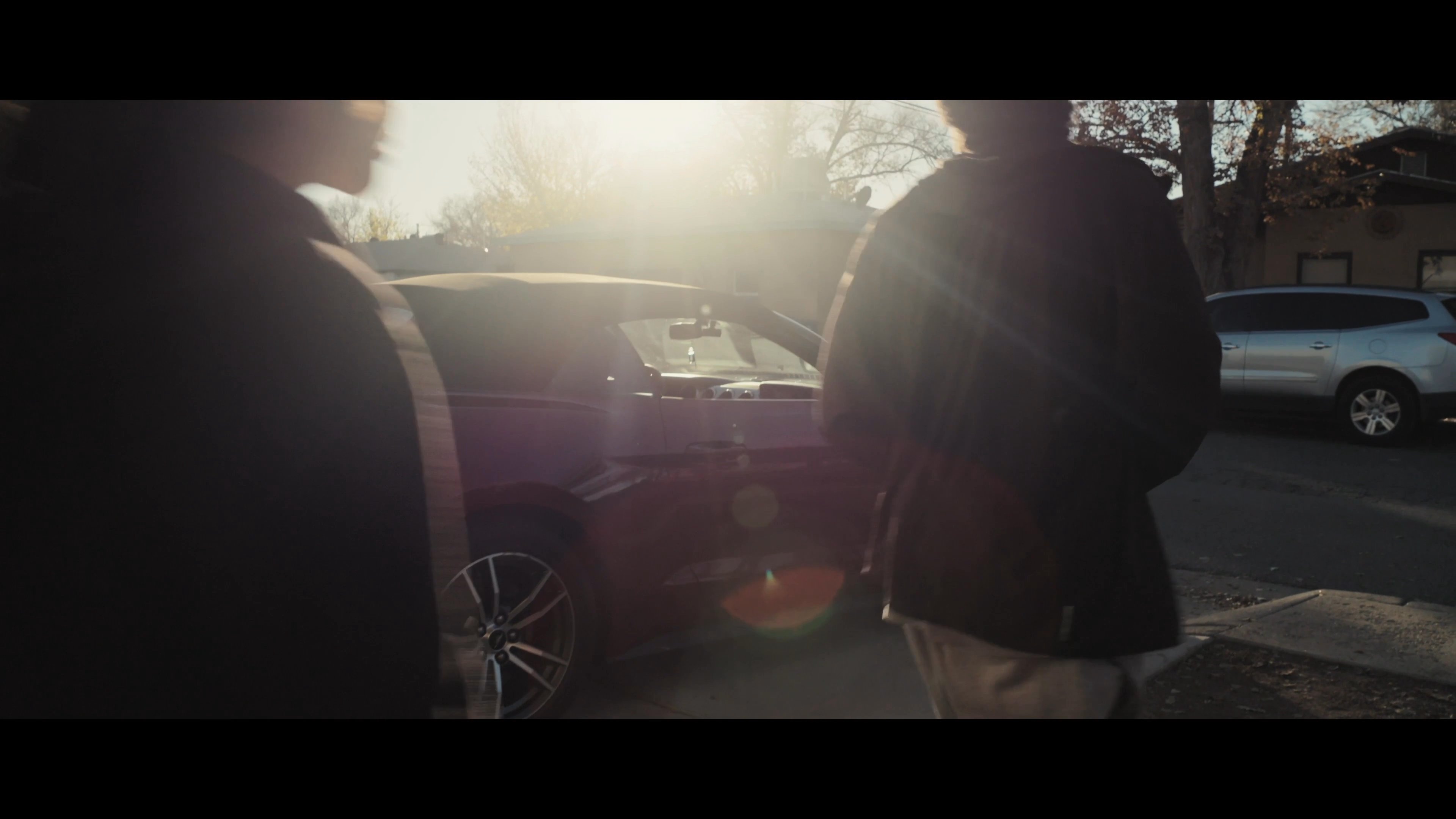 A group of young adults concludes a discussion inside a garage before exiting to a parked convertible during the golden hour.