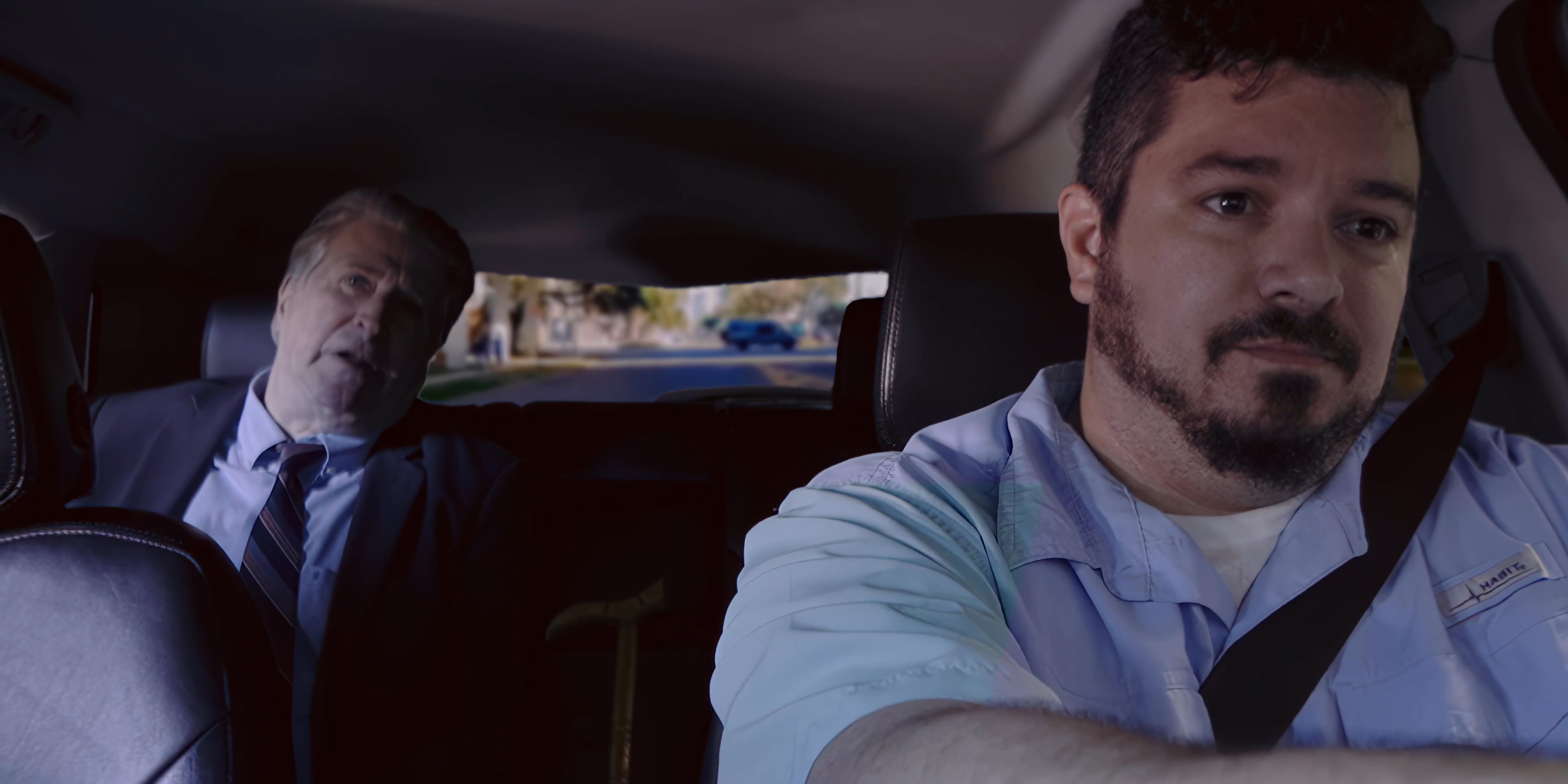 A driver and passenger engage in dialogue while traveling through a residential area during a vehicle commute. The interaction captures a typical professional transit setting.