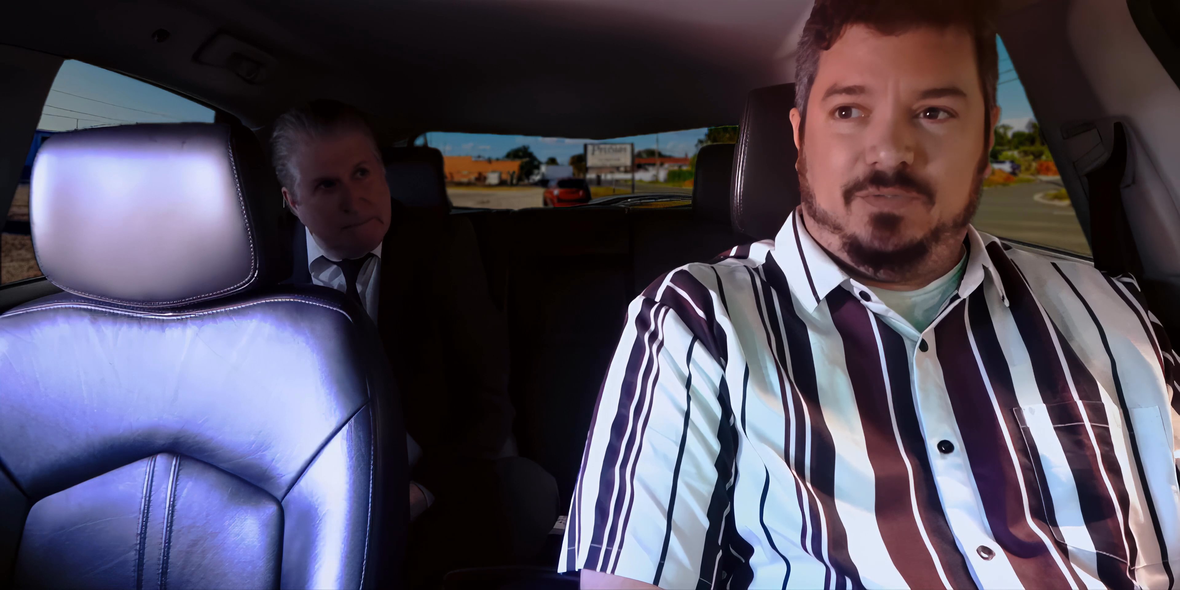 Two men engage in a serious conversation while sitting in the front seats of a parked vehicle.