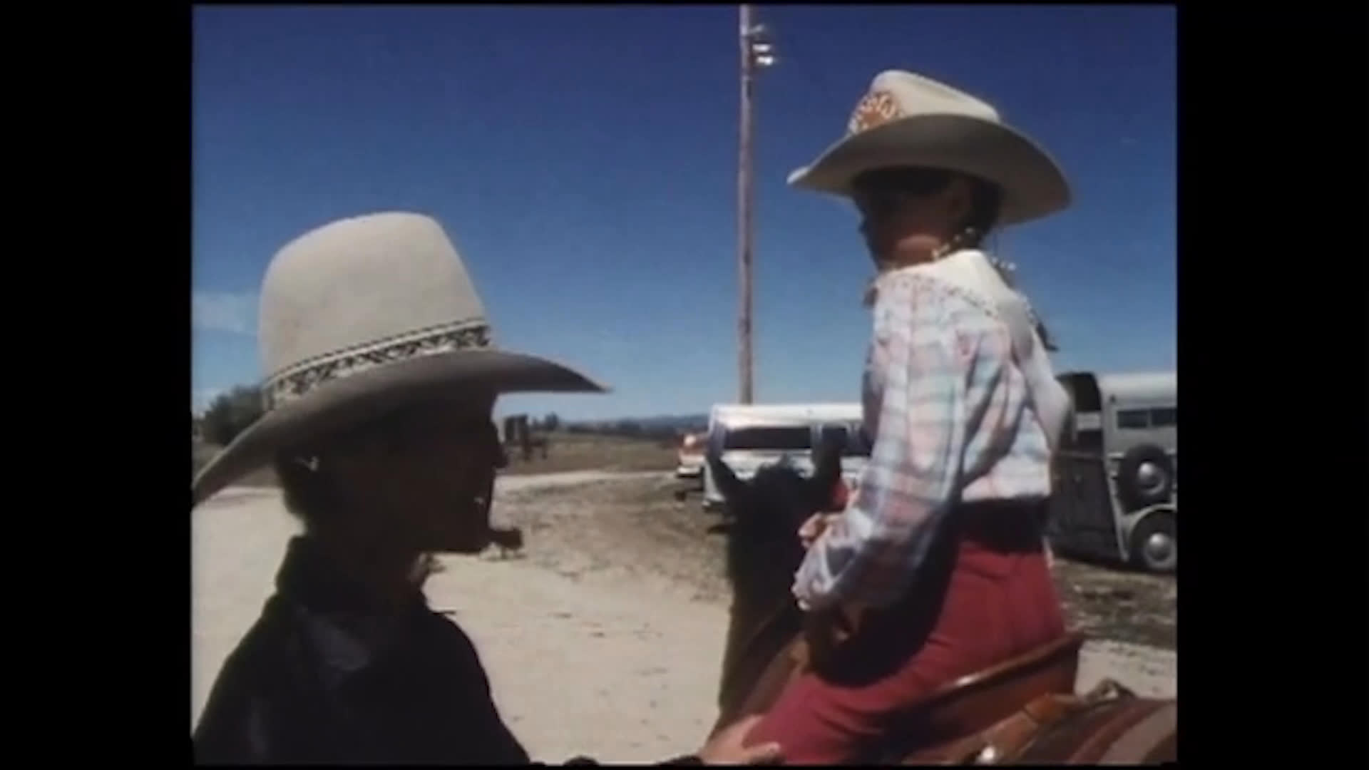A young rider sits astride a horse in a dusty outdoor arena while another person offers advice about working as a team and staying aware of the horse. She says she plans to compete in barrels and poles.