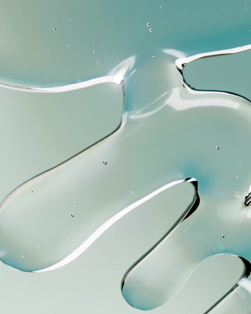 Macro shot of clear gel-like liquid with air bubbles on a soft mint and blue surface