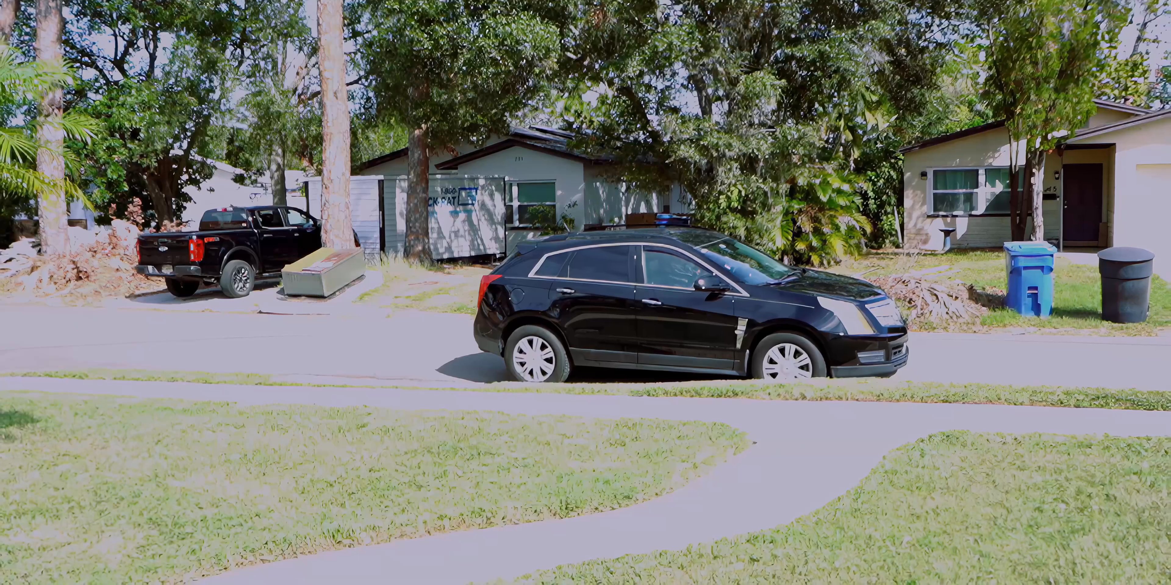 A black SUV drives down a suburban street and pulls up to a house. A man approaches the front door and knocks, waiting for a response.