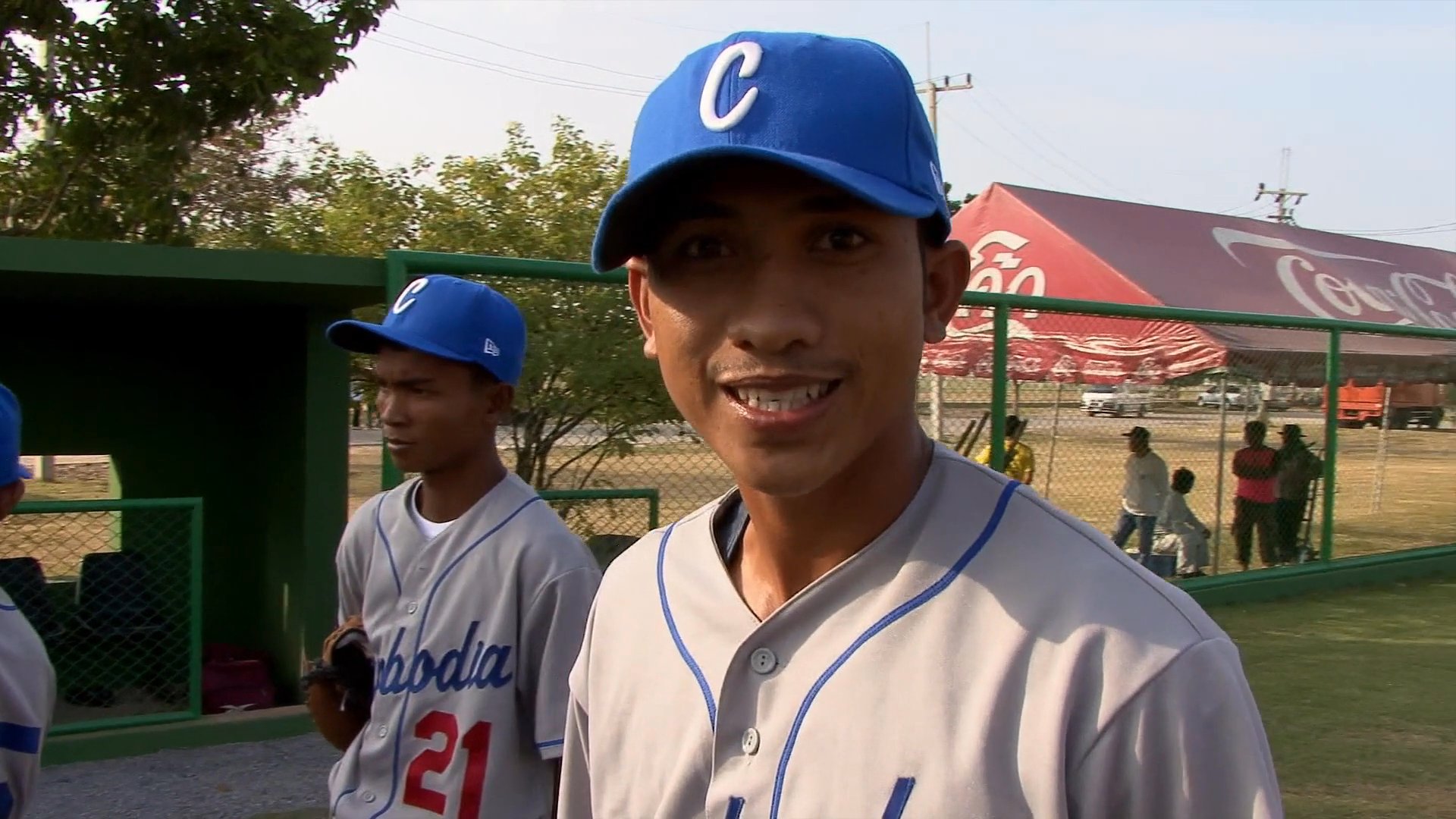A coach provides guidance to a youth baseball team on the field, offering instruction and demonstrating techniques to players in team uniforms.