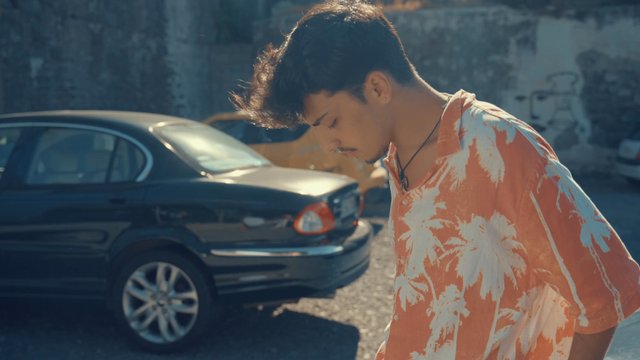 A teenage boy leaning against the hood of his car