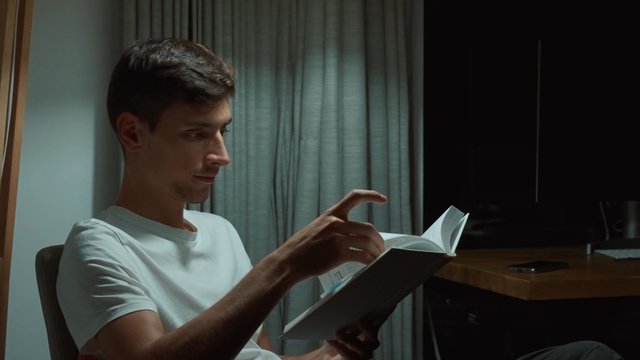 Un hombre está leyendo un libro con atención por la noche.