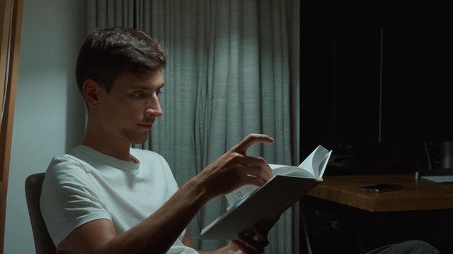 A man carefully reading a book at night