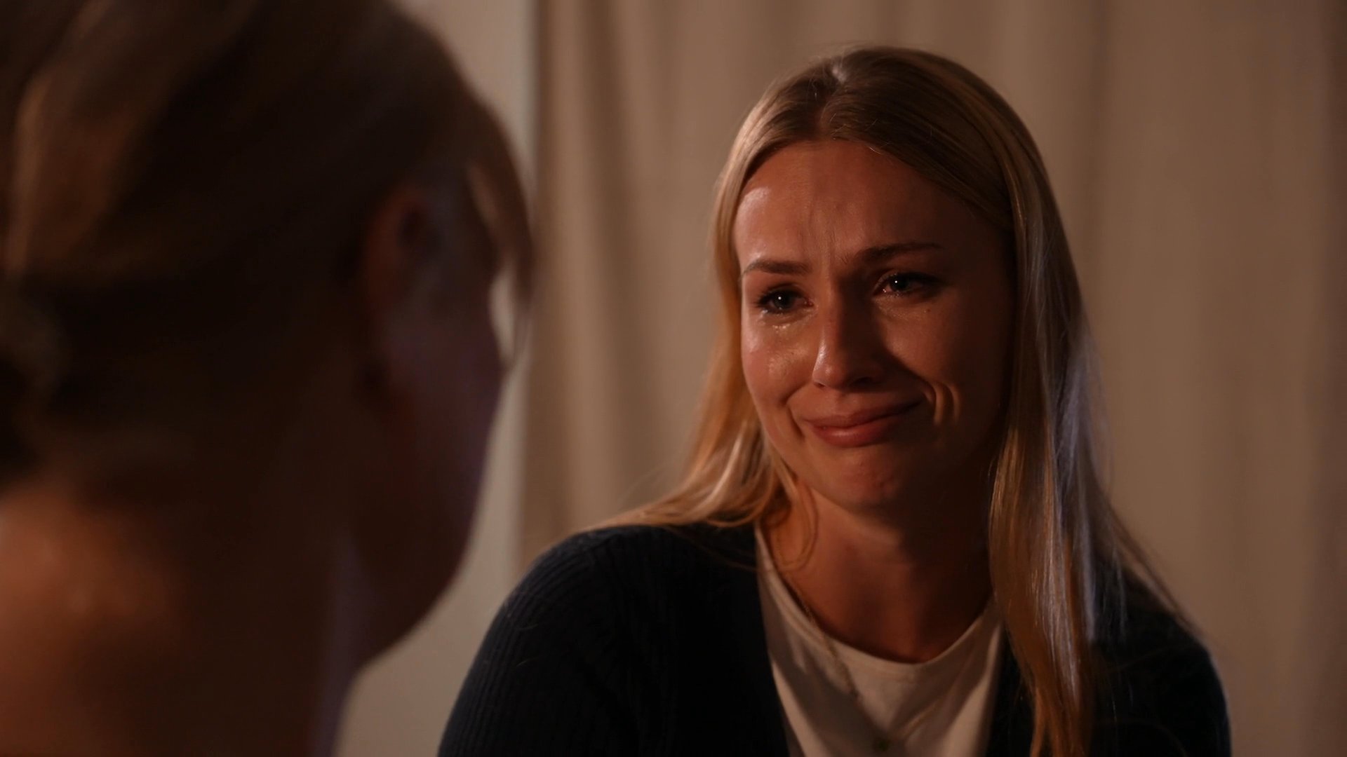 An older woman offers emotional comfort and support to a younger woman during a deeply personal and intimate conversation. The two exchange supportive gestures and expressions in a quiet, softly lit setting.