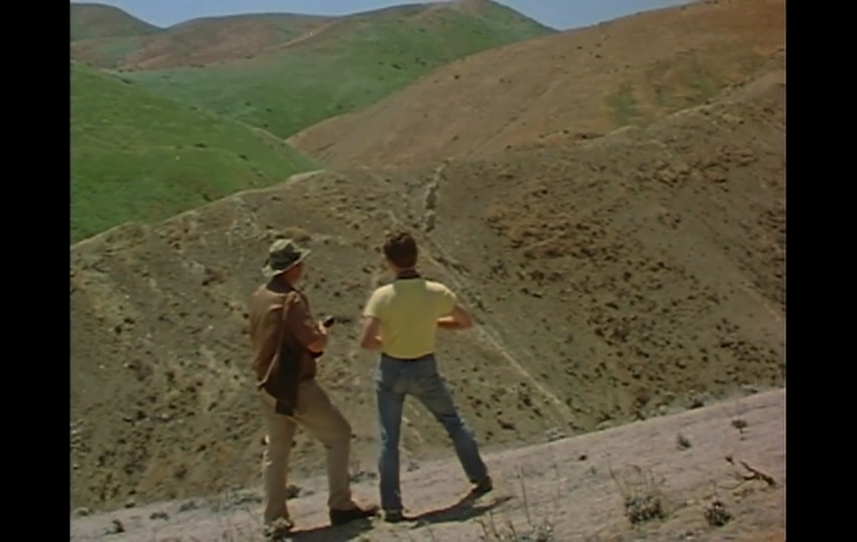 Cattle graze across open range as campers and other visitors gather near vehicles and explore dry, brush-covered terrain. The narration argues that removing livestock grazing from public land could protect stream banks and cultural sites such as arrowhead locations.