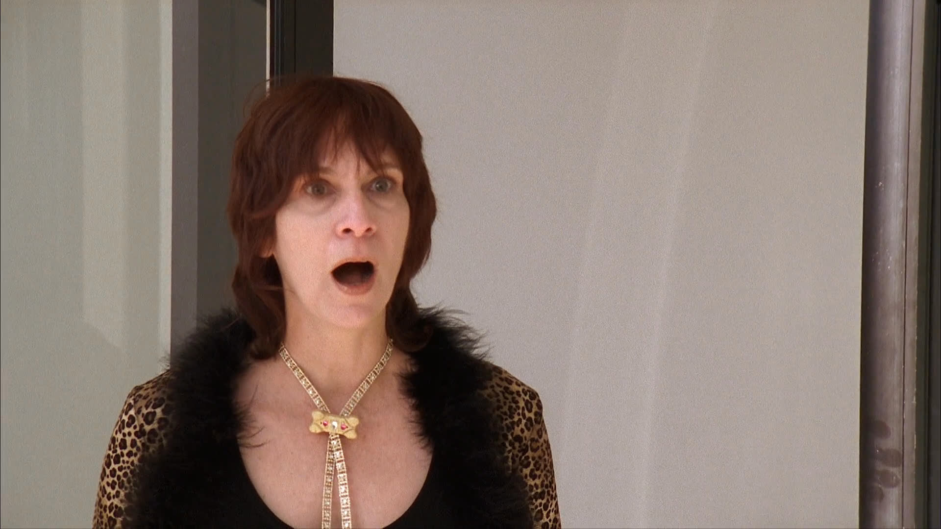 A woman in a leopard print top interacts with an individual wearing a brown dog mask who is smoking. The surreal scene captures the woman's shocked expression as she brushes smoke away from the costumed figure.