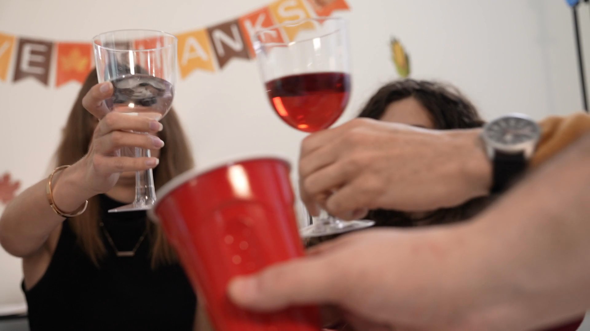 Friends and family socialize and share toasts at a Thanksgiving-themed indoor gathering. The scene transitions between candid interactions at the party and a pensive moment with an individual drinking from a mug.