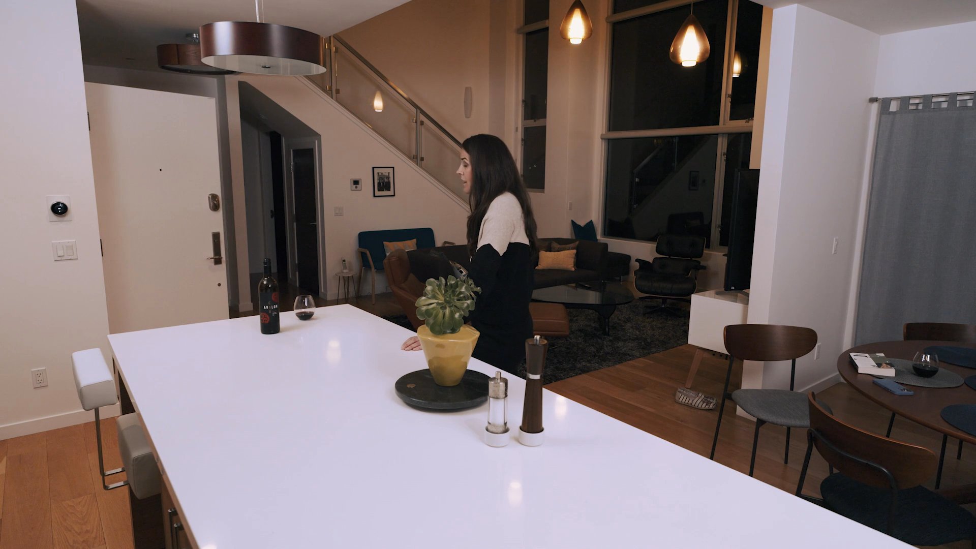 A man and woman engage in a heated discussion in their home before the man departs, leaving the woman visibly distressed and alone. She eventually attempts to find solace in a book at the dining table.