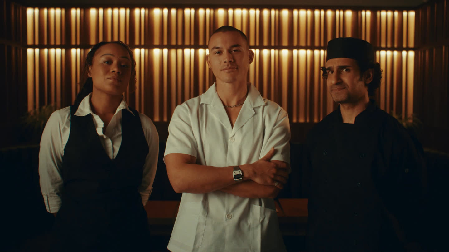 Film still: three hospitality workers facing the camera in a restaurant