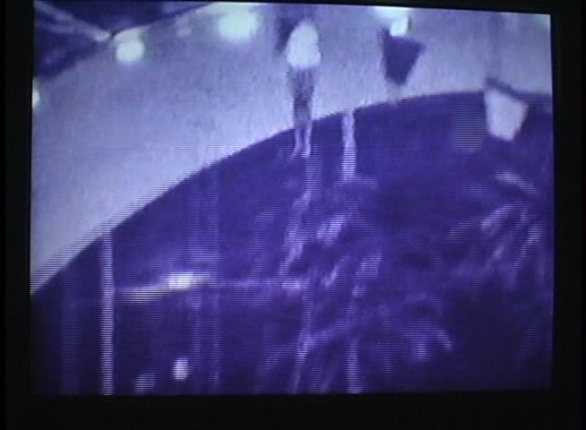 An elderly speaker provides commentary on vintage 'Plunge Carnival' aquatic shows while archival black-and-white performance footage displays acrobatic stunts and water-based spectacles.