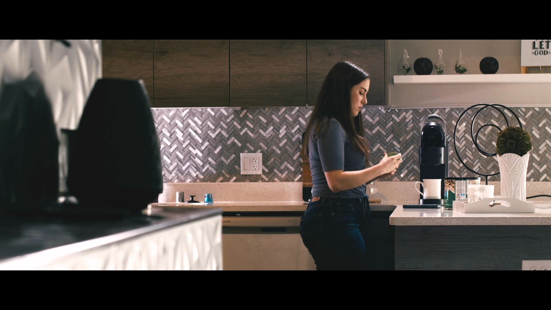 A woman prepares a cup of coffee using a countertop machine in a modern residential kitchen. She carefully manages the brewing process before adjusting the machine settings.
