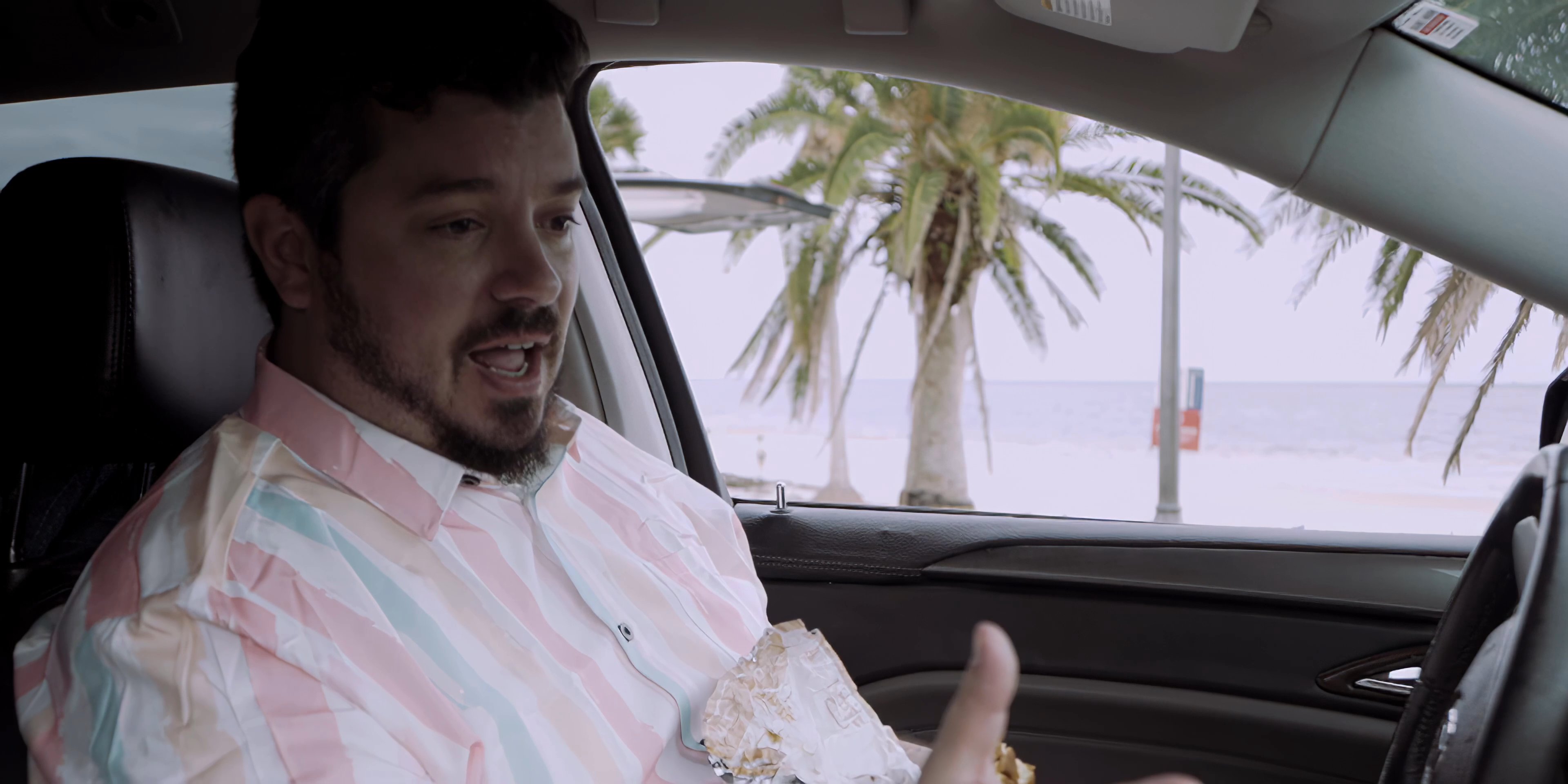 A man in a vehicle engages in a video call with a woman, facilitating a remote conversation from a tropical location.