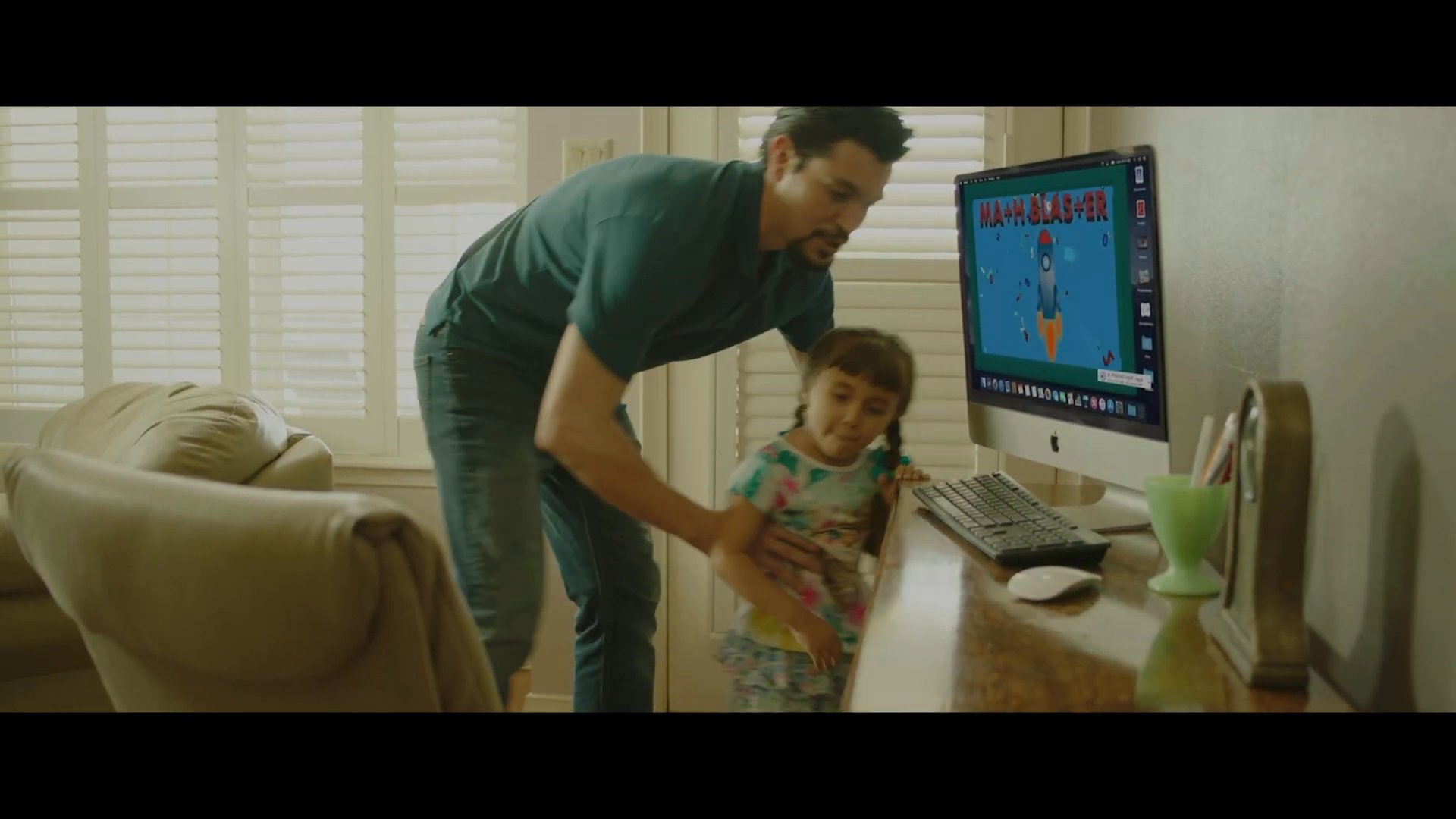 A father spends quality time with his young daughter, guiding her at a computer to engage with educational content. The scene highlights a warm, supportive atmosphere as the child explores digital learning.