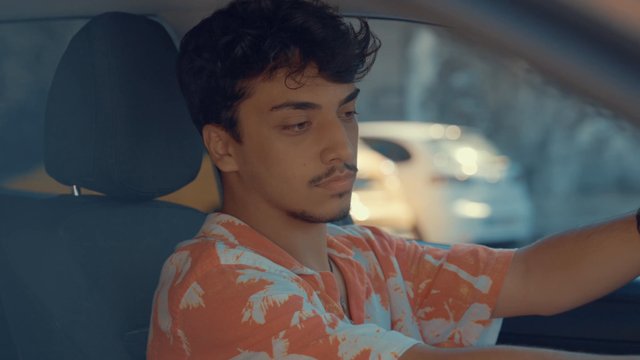 A teenage boy sitting in his car and bopping his head to music