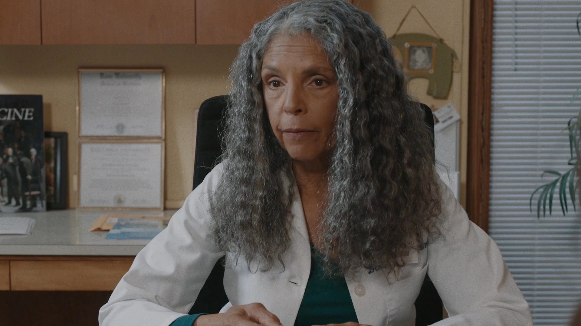 A physician conducts a serious medical consultation with a couple in a clinical office setting. The participants engage in detailed professional dialogue regarding healthcare concerns.