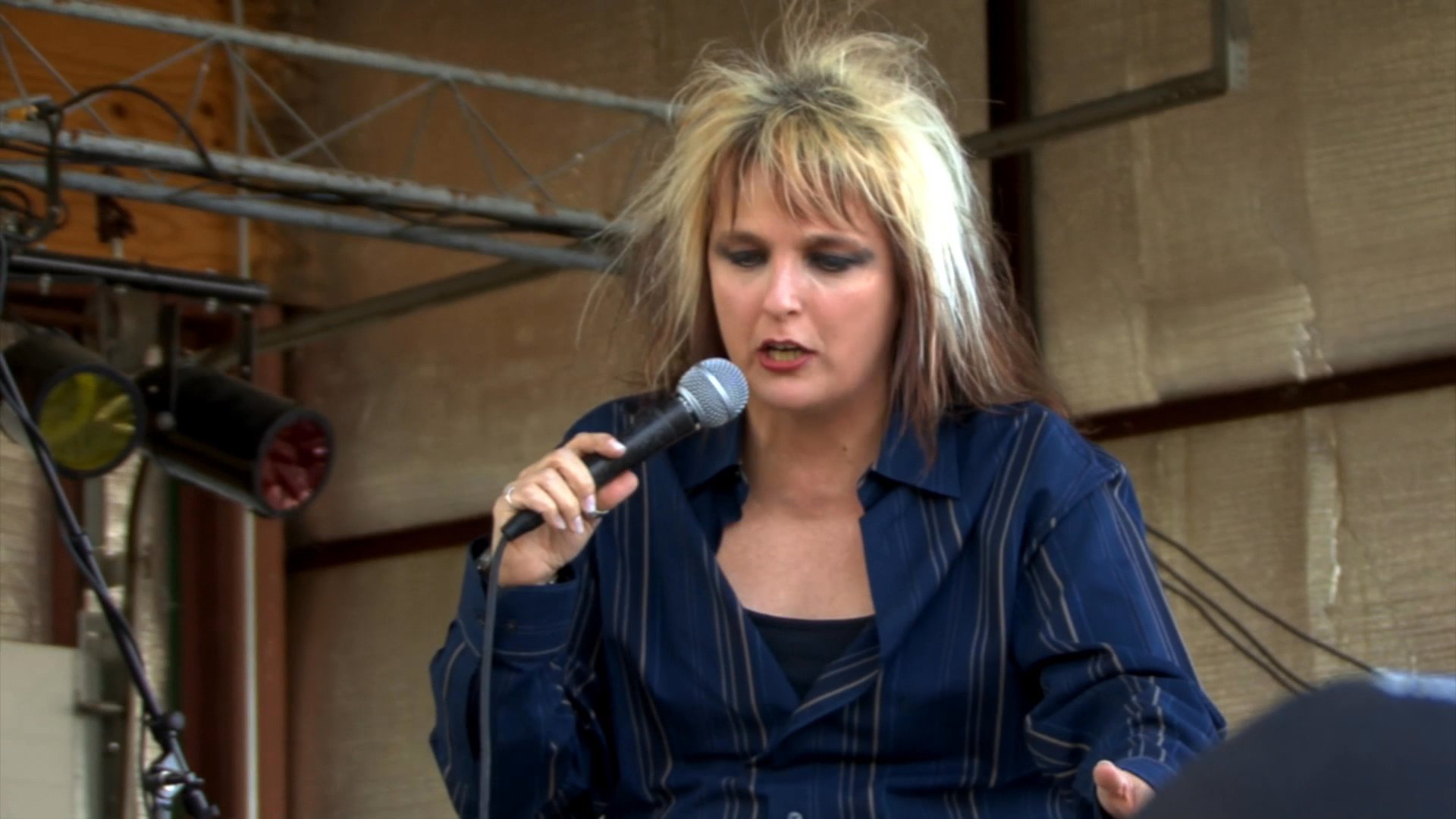 A female rock vocalist performs on an outdoor stage for an enthusiastic audience. She sings expressively while engaging with the crowd during a live musical event.
