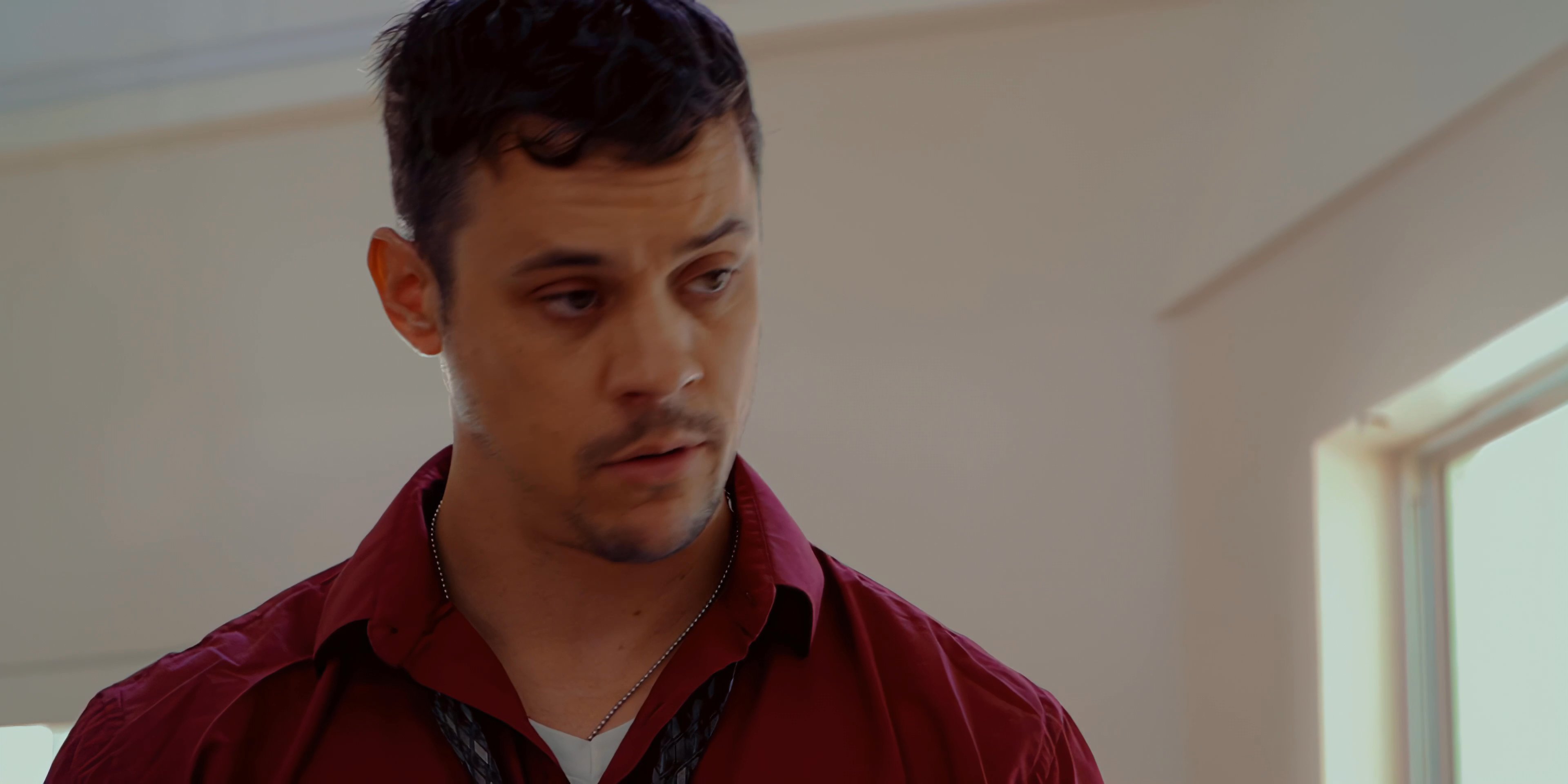 A man in a red shirt speaks directly to an audience, displaying focused engagement and clear verbal communication within a bright indoor setting.