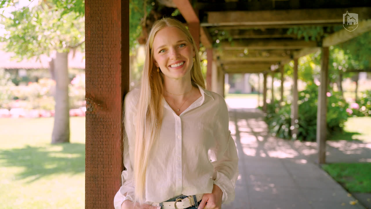 Briar Blake smiling, standing under a shaded arbor on campus.