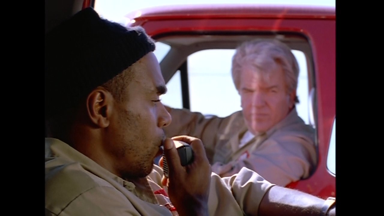 Two individuals engage in a conversation while traveling in the cab of a red truck. The driver maintains focus on the road as the passenger speaks, highlighting a moment of interaction during a journey.