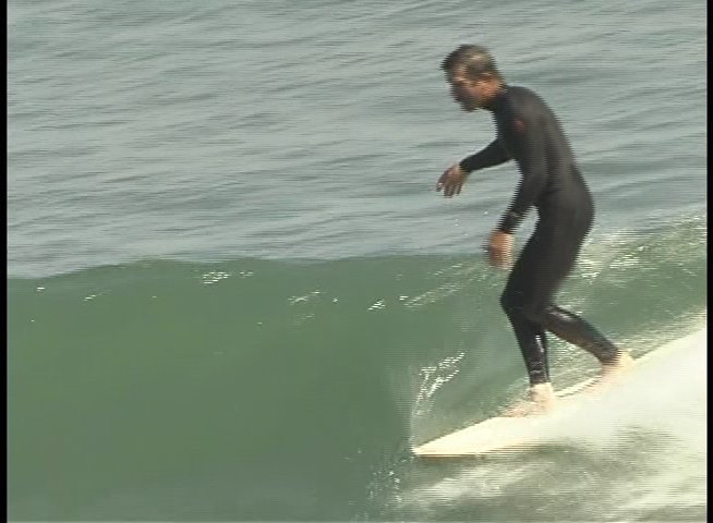 A surfer in a wetsuit maneuvers a longboard across an ocean wave, demonstrating balance and control. The sequence highlights the fluid movement and technical adjustment throughout the ride.