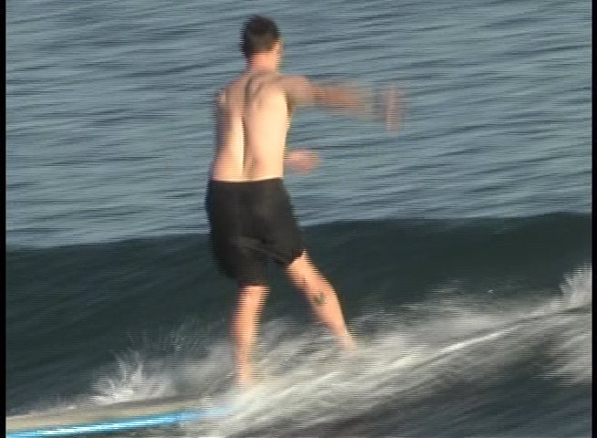 Surfers demonstrate cross-stepping maneuvers on longboards while riding waves in the ocean.