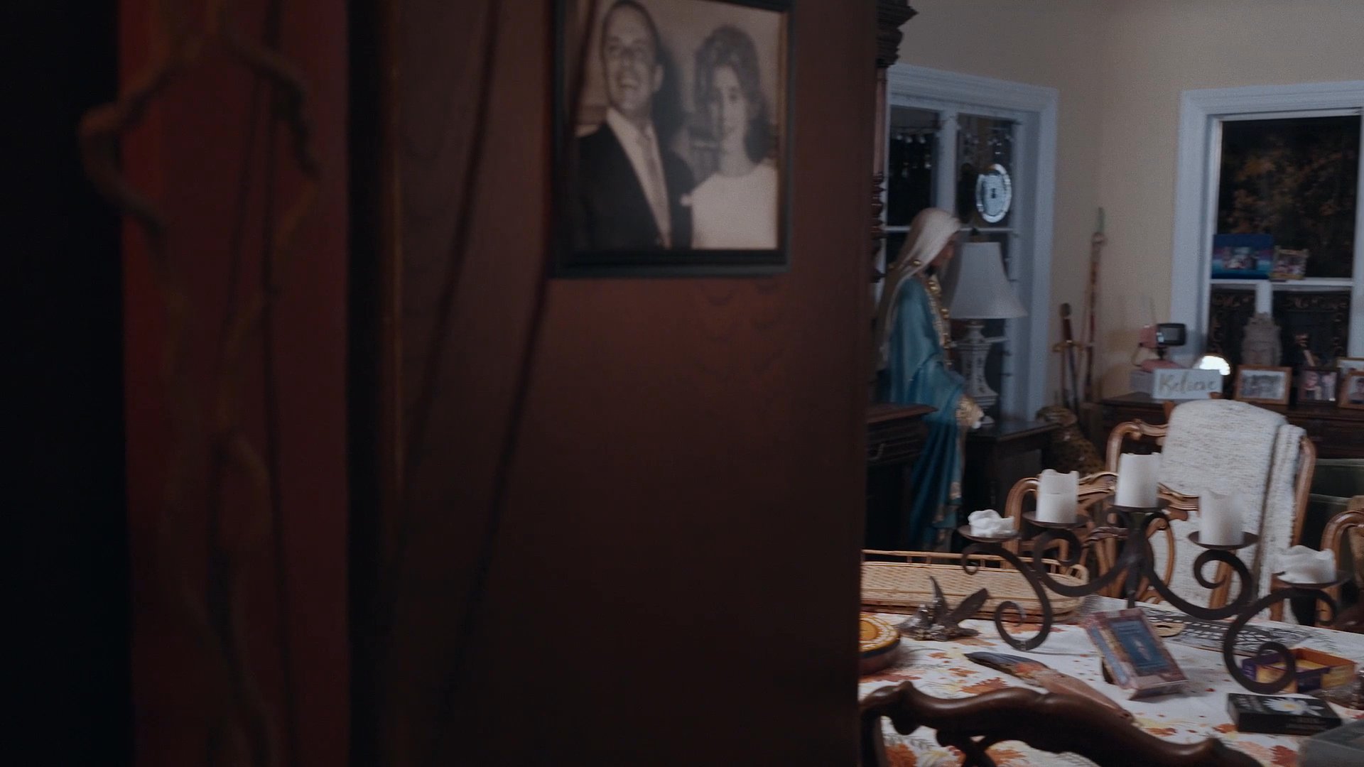 A man enters a dimly lit, furnished living room through a decorative door and proceeds to walk further into the home interior.