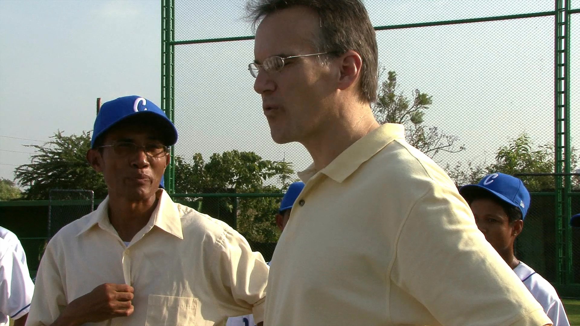 Major League Baseball executive Jim Small oversees a baseball practice session, providing instruction to players on an outdoor field.