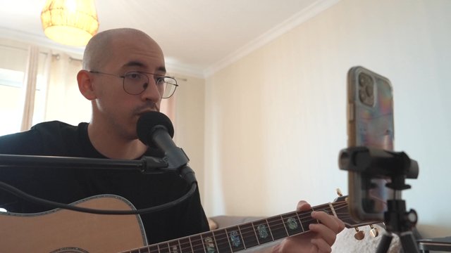 A guy singing a song and playing a guitar in a home studio