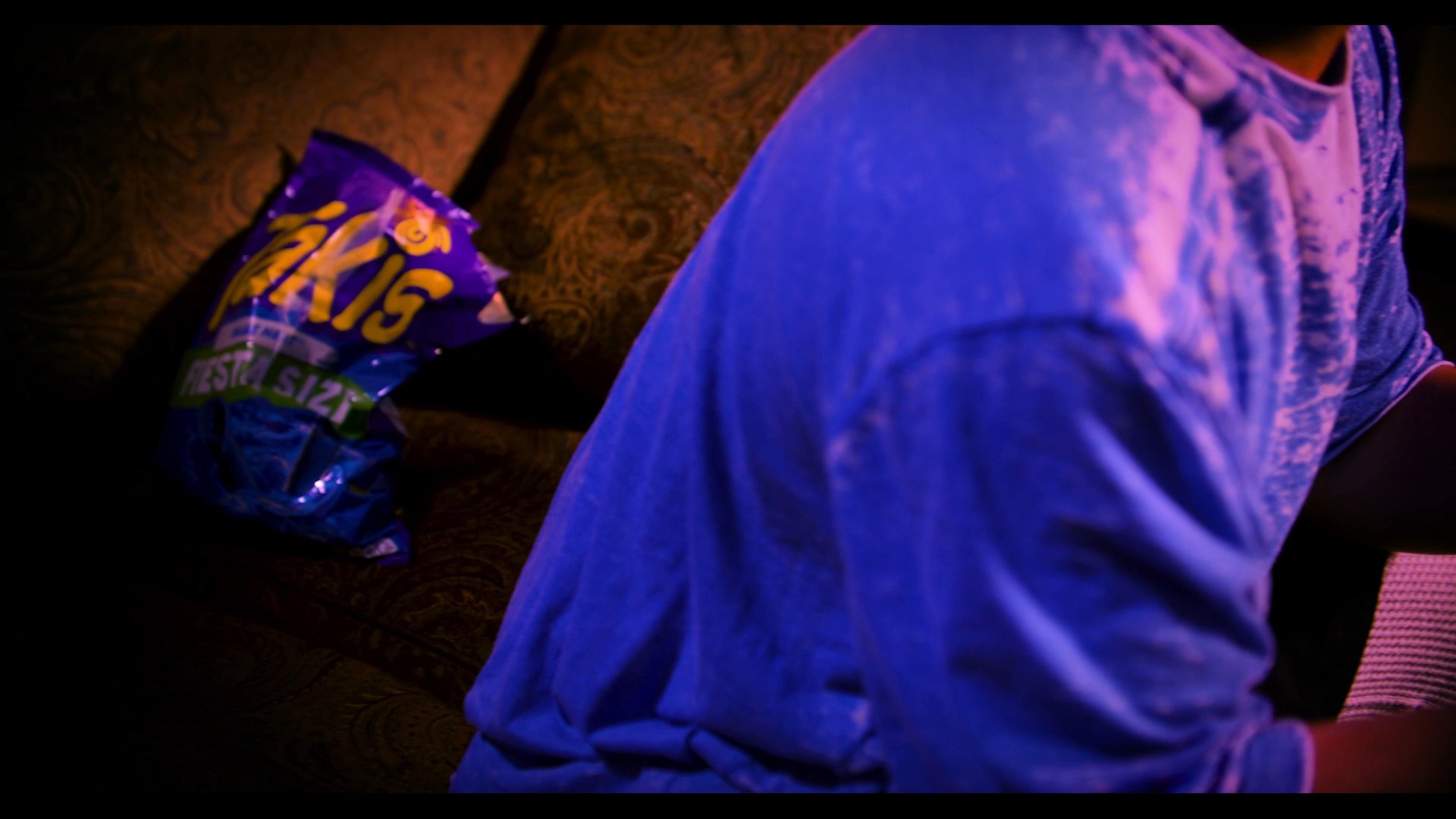 A gamer sits on a sofa, distracted by a psychic reading in a crystal ball while snack bags sit nearby. The scene highlights the juxtaposition of mystical intervention and casual lifestyle habits.