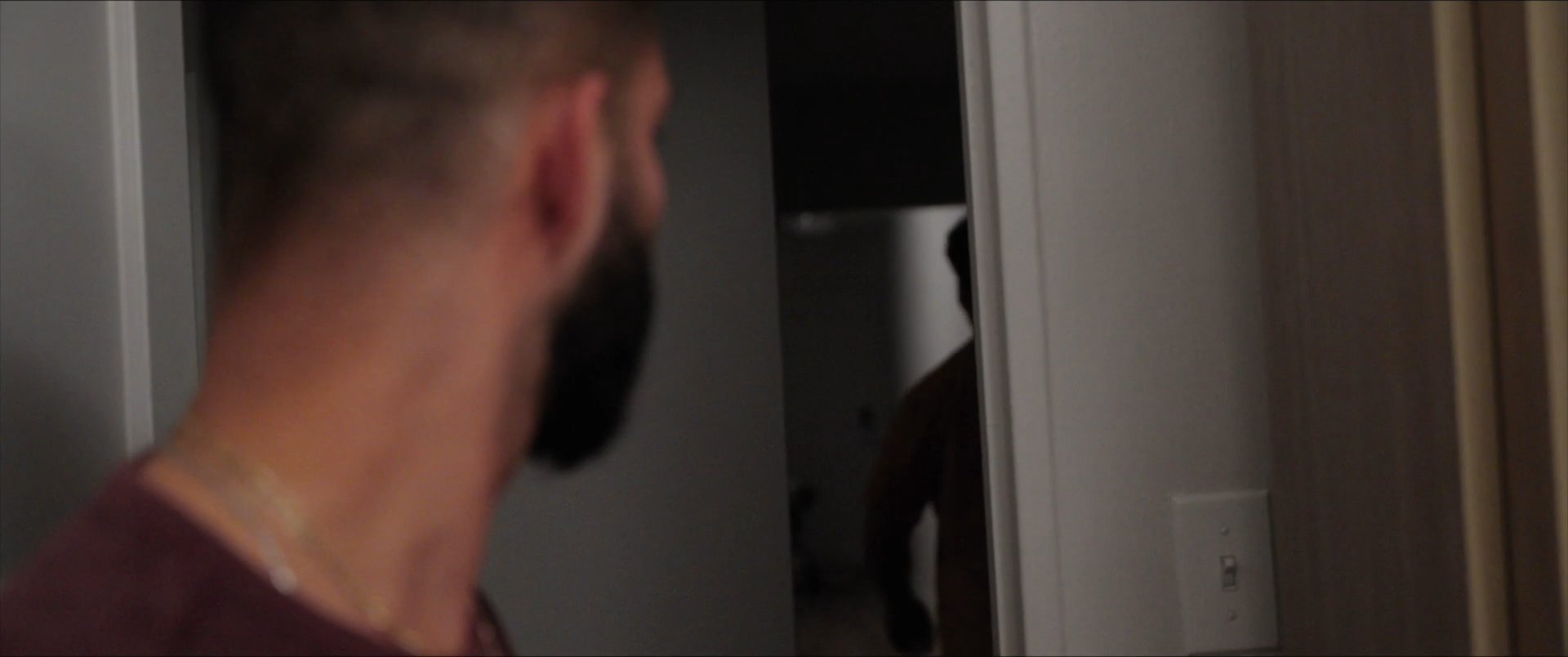 A man draped in a towel exhibits visible signs of distress and anxiety while sitting in a bathroom, briefly interrupted by the presence of another man at the doorway. He subsequently attempts to compose himself by covering his face with his hands.