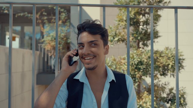 A man laughing with his friend on a phone call while sitting in the shade