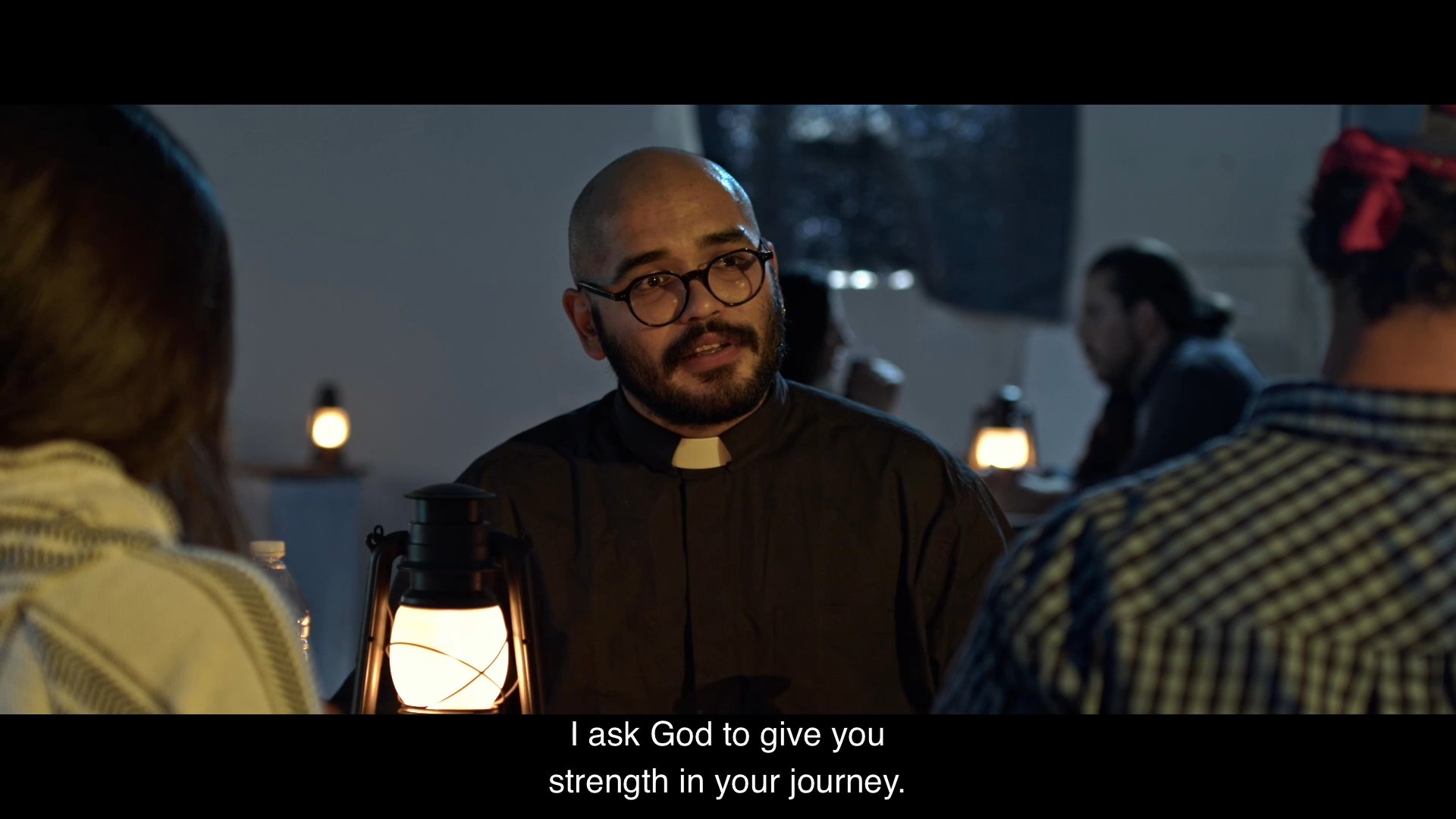 A priest offers shelter and spiritual comfort to two individuals in a dimly lit, lantern-lit room. The guests express gratitude and offer a small token of appreciation to the church in return for his kindness.