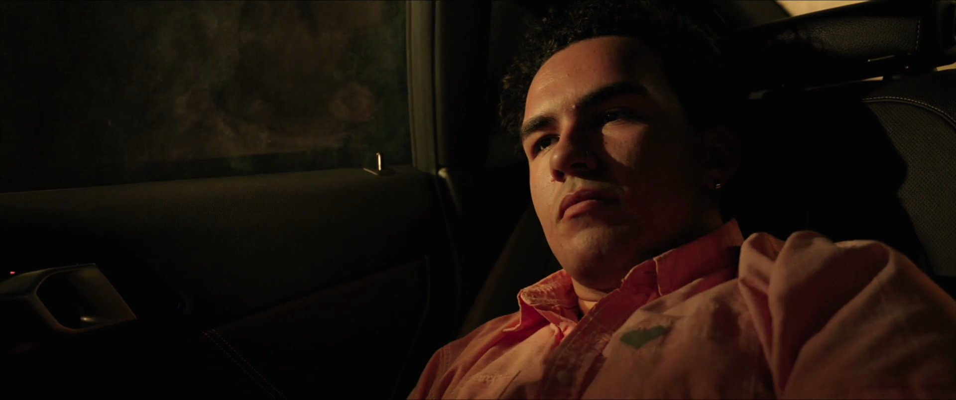 A man sits in the passenger seat of a vehicle at night, looking at a photo on his smartphone before gazing out the window.