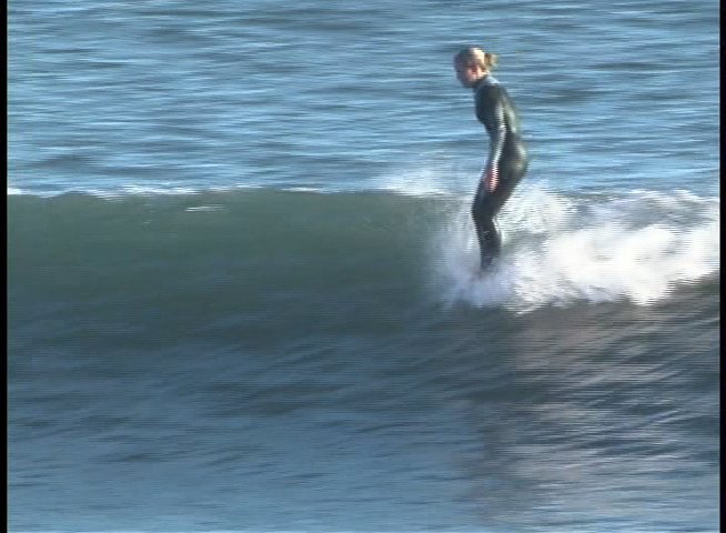 A surfer in a wetsuit skillfully navigates the face of an incoming ocean wave. The athlete maintains balance and momentum while traversing across the rolling water.