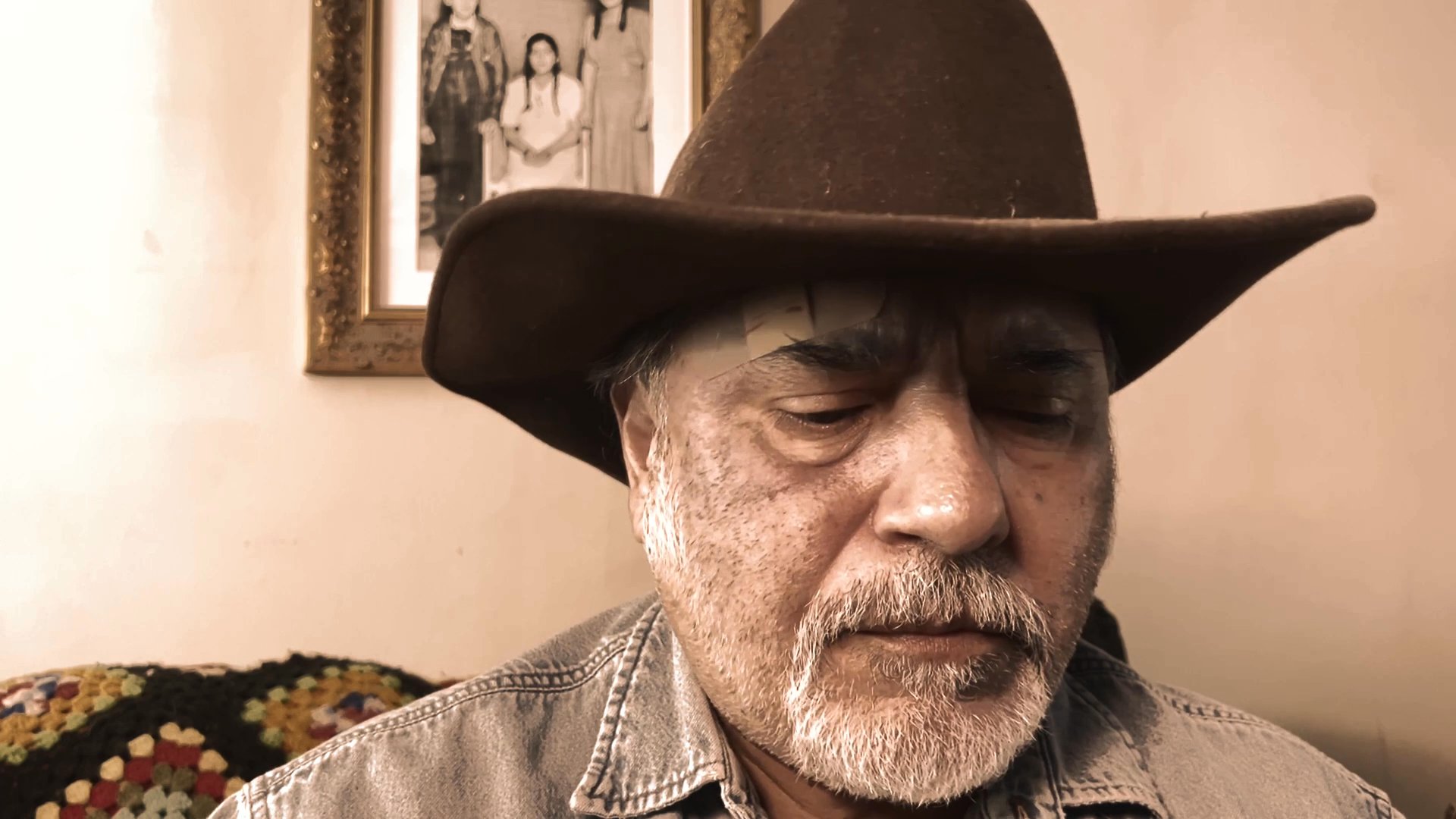 A mature man wearing a brown cowboy hat delivers a direct address while looking toward the camera.