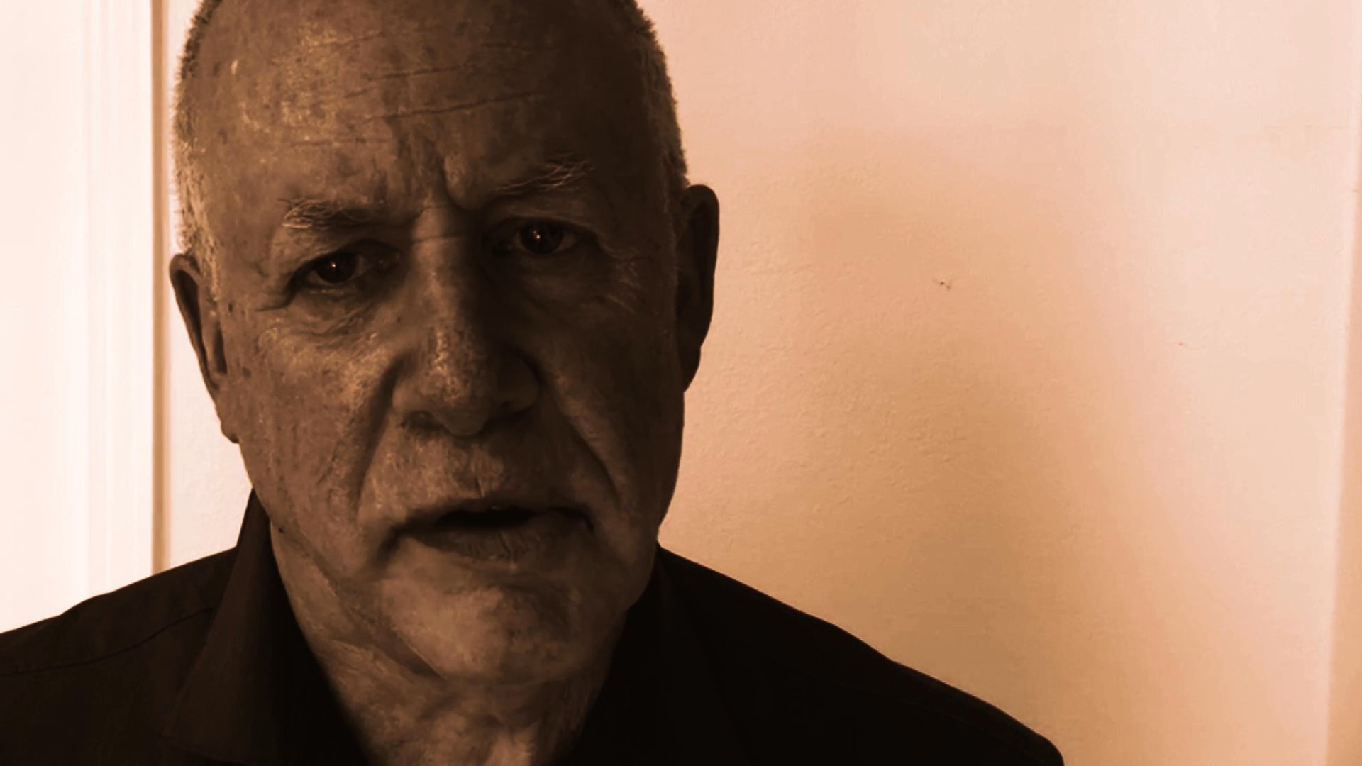 An older man delivers a direct, serious message to the camera against a neutral background. The presentation utilizes a sepia-toned aesthetic to emphasize the subject's commentary.
