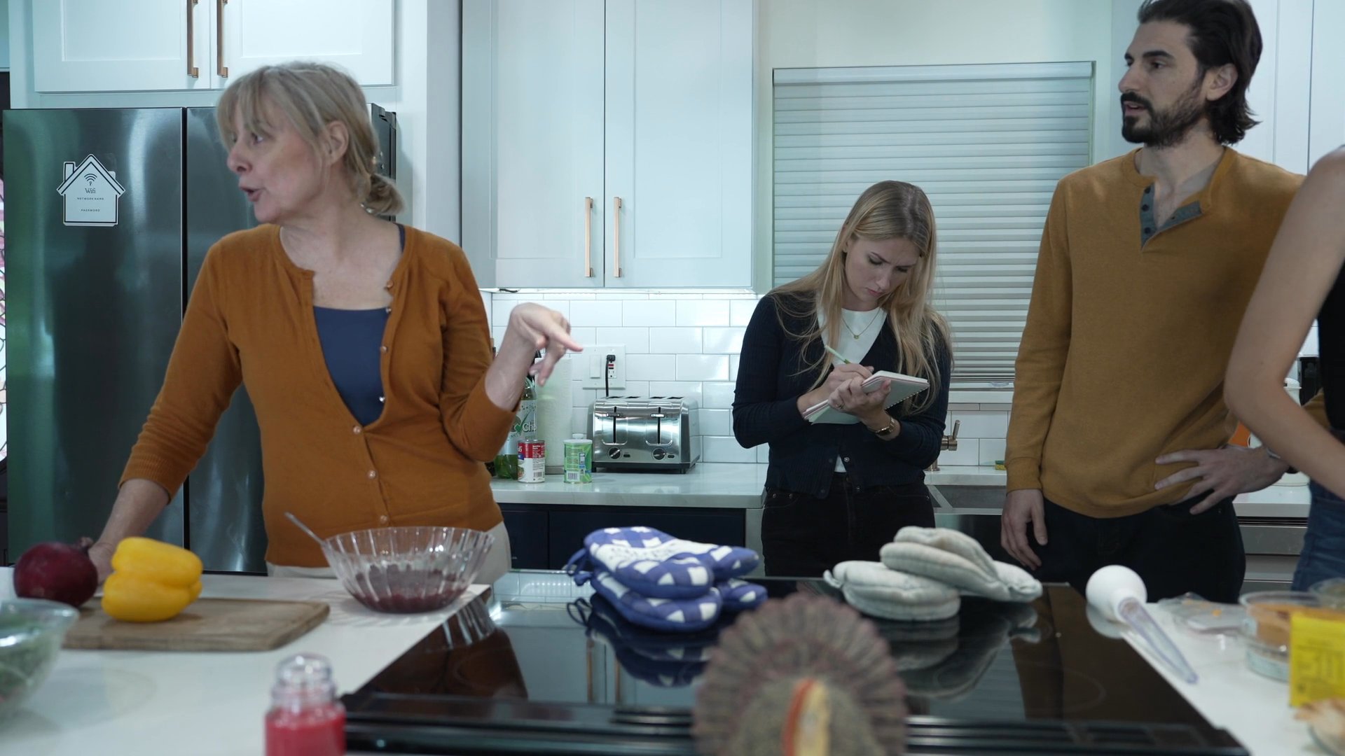 A group coordinates tasks in a residential kitchen while preparing a meal, utilizing written notes and verbal communication to manage workflow. The team members engage in active discussion, establishing clear roles and procedures within the workspace.
