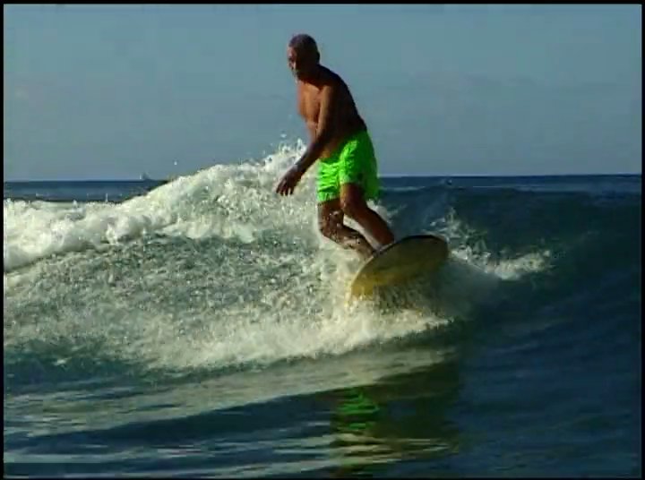 Surfers navigate waves along a tropical coastline, followed by a tribute to the legacy of Duke Kahanamoku through vintage imagery.