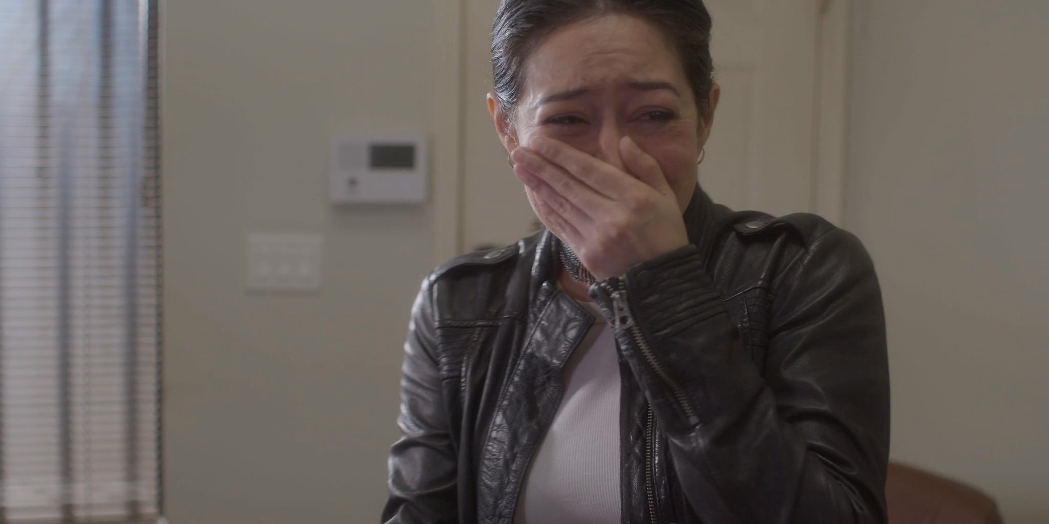 A woman experiences intense emotional distress while viewing a photograph of two people in a residential setting. She breaks down in tears as she reflects on the image in her hands.