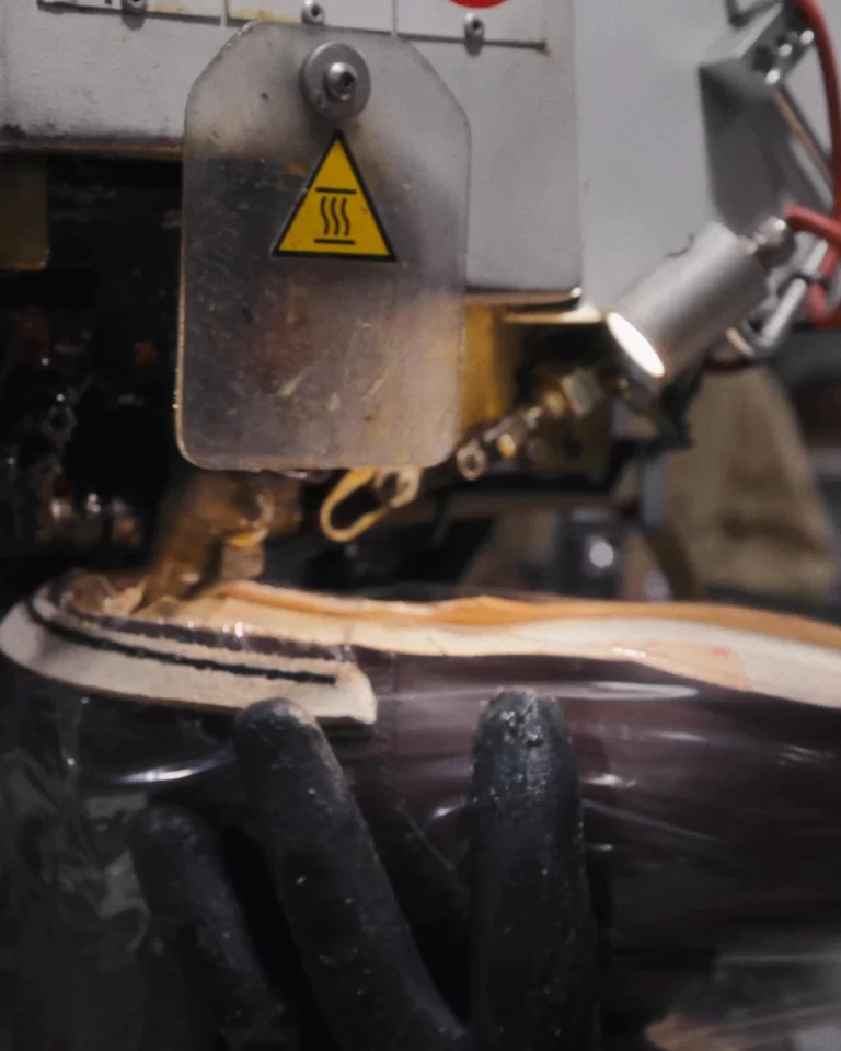 Closeup video of man using a machine to hand stitch the sole construction of a boot