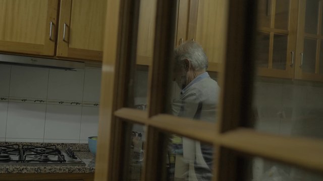 Old man's reflection in the glass as he makes coffee